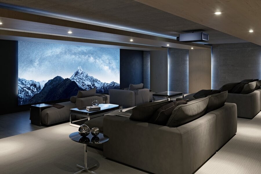 A luxurious cinema featuring gray couches facing towards a large screen. 