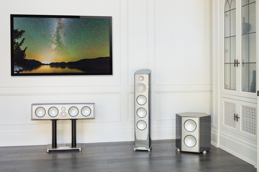 three Paradigm Persona speakers sitting on the floor below a wall-mounted 4K TV.