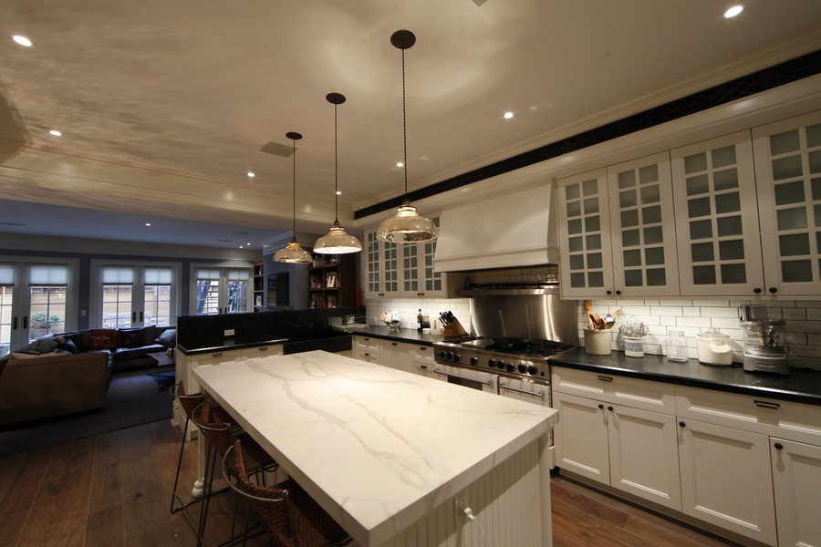 A beautiful kitchen with three pendant lights, in-ceiling lights, and under-cabinet lights.