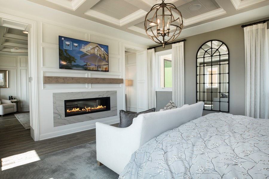 Bedroom with a small couch at the foot of the bed facing a fireplace and wall-mounted TV showing the Control4 interface.