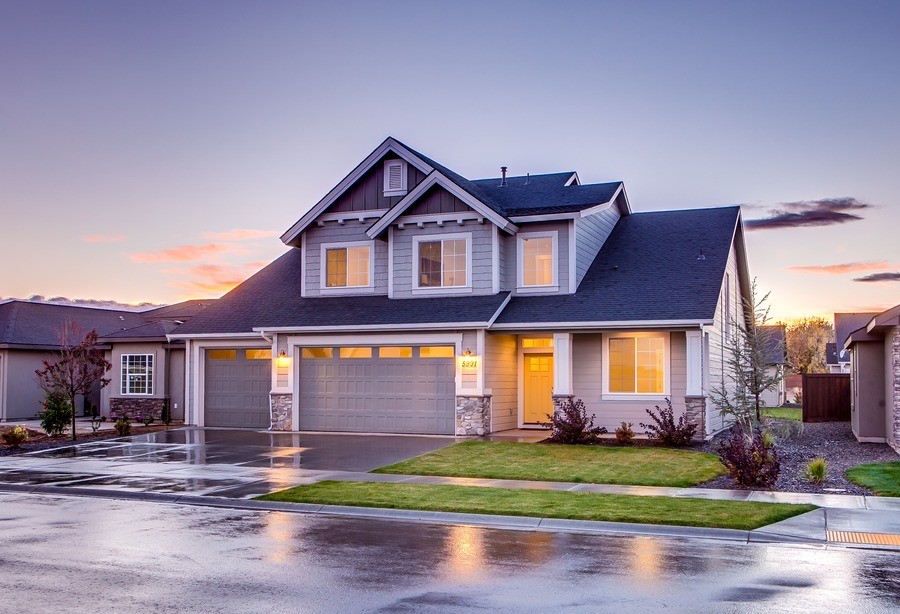 Photo of a beautiful gray home with rainwater on the street and in the driveway, lit from the inside. 