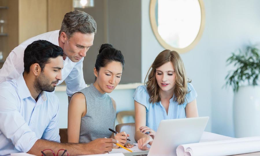 four people huddled around a laptop looking at the screen