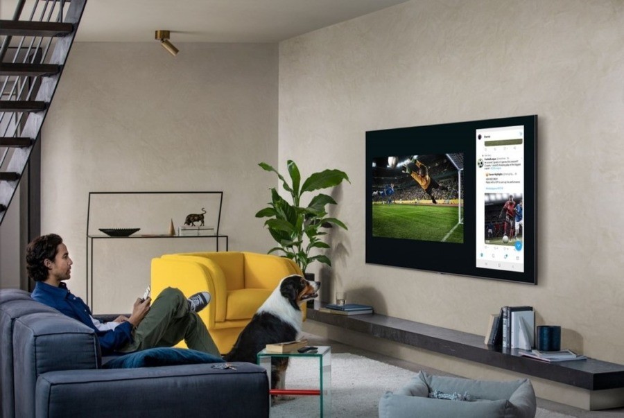 A man and his dog watching a wall-mounted TV in a small media room.