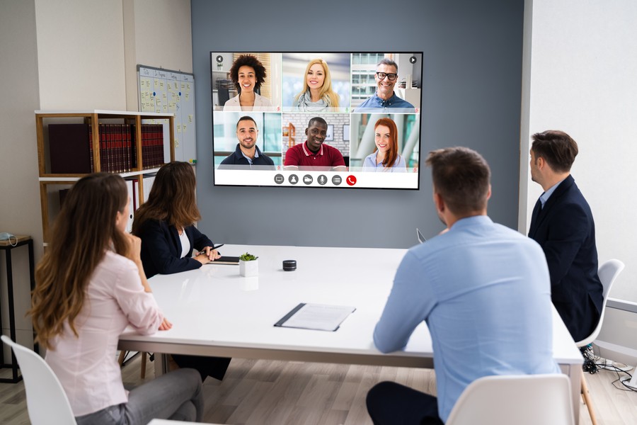 People sitting at a conference room watching a split-screen video conference on the display. 